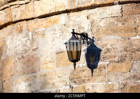 a hinged streetlight lantern from black iron on the background of a stone wall of shell rock. Stock Photo