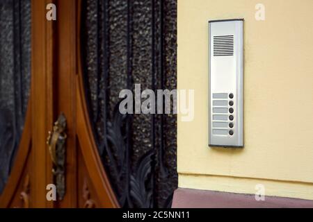 An intercom with a microphone and call buttons close-up on a yellow wall at the entrance wooden door with glass and a wrought-iron grille. Stock Photo