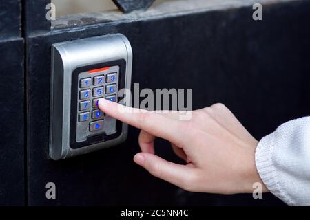 female hand dials the access code on the electronic lock by pressing a finger with a blue backlight, close-up of the security lock with the hand. Stock Photo