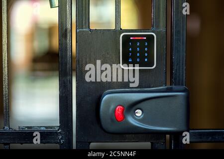 A security lock on an iron gate with a touch panel for access by an access code key or a classic key in the keyhole with a red button for opening. Stock Photo