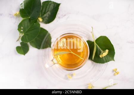 Transparent tea cup with linden tea and linden flowers and leaves on a white marble table as background. Top view Stock Photo