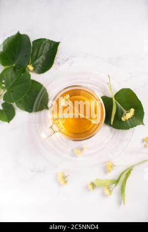 Transparent tea cup with linden tea and linden flowers and leaves on a white marble table as background. Top view Stock Photo