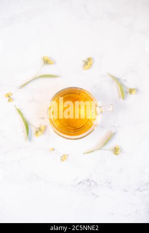 Transparent tea cup with linden tea and linden flowers on a white marble table as background. Top view Stock Photo