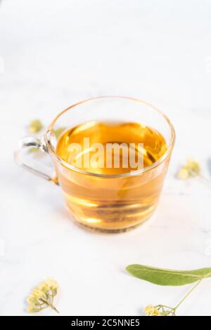 Transparent tea cup with linden tea and linden flowers on a white marble table as background Stock Photo