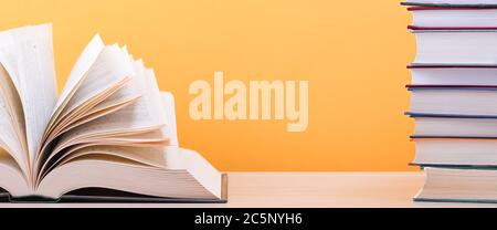 A large, thick hardcover book is lying on a light wood table. The book is open, next to a stack of closed books, and on the back is a yellow backgroun Stock Photo