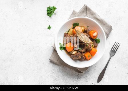 Beef meat stewed with potatoes, carrots and spices on white background, top view. Homemade winter comfort food - slow cooked meat stew in bowl. Stock Photo