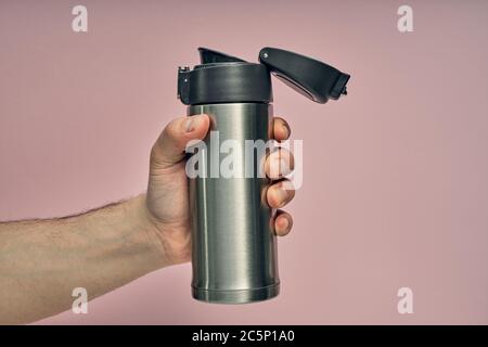 Metal mug thermos in hand on a colored background. Hot drinks on the go. Thermo mug. Stock Photo