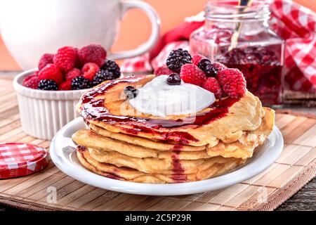 Pancakes with cream, raspberries, and blackberries on the wooden table. The concept of healthy eating and nutrition. Stock Photo