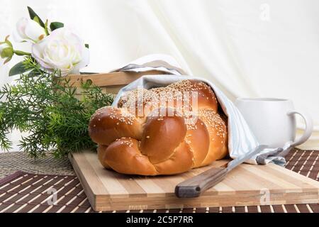 a braided loaf of sesame egg bread on a wooden cutting board with a knife isolated on white Stock Photo