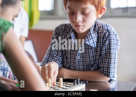 Serious chess player kid thinking and moving coin at home - Concept of kid concentration of game during Early development, home educational games for Stock Photo