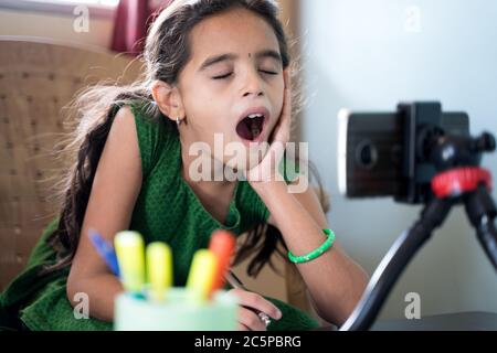Sleepy boredom kid yawning during online class infront of mobilephone - concept of tired or bored child during homeschooling, online education at home Stock Photo