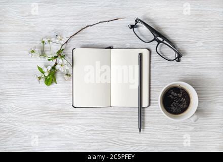 Stationery set. Blank notebook, coffee cup, pencil, glasses and flower on light wood table background. Flat lay. Stock Photo
