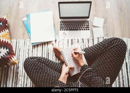 Businesswoman dressed pajamas writing day plan enjoying morning coffee on living room floor office with laptop, papers and other stuff top view shot.D Stock Photo