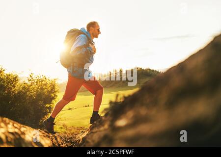 Backpacker traveler in trekking boots jumping over the ditch on mountain dirty path at summertime sunny day side shot image. Stock Photo