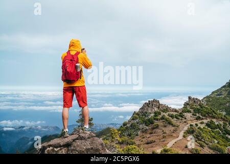 Young adult caucasian man dressed  sporty clothes with backpack taking a picture from Pico Ruivo mount 1861m - the highest peak on the Madeira Island, Stock Photo