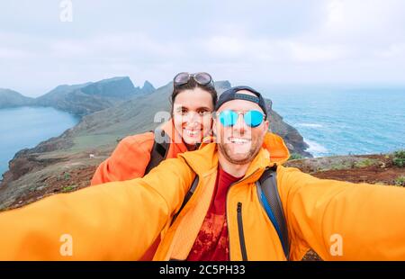 Smiling brightly dressed backpackers couple taking selfie portrait as they hiking and enjoying Atlantic ocean view on Ponta de Sao Lourenço peninsula Stock Photo