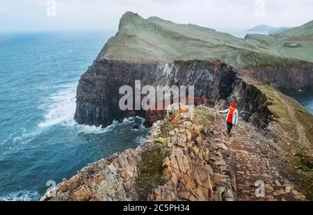 Young female backpacker hiking by footpath on Sao Lourenco headland with Atlantic ocean bay view in the end of February, Madeira island, Portugal. Act Stock Photo