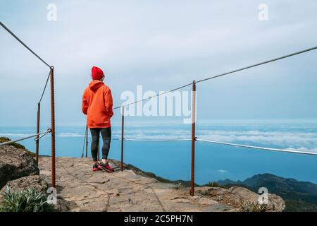 Young adult caucasian female dressed sporty clothes standing on the path and enjoying clouds view from Pico Ruivo mount 1861m - the highest peak on th Stock Photo