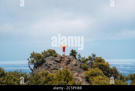 Young adult caucasian man dressed  sporty clothes with red backpack rising up hands enjoying view from Pico Ruivo mount 1861m - the highest peak on th Stock Photo