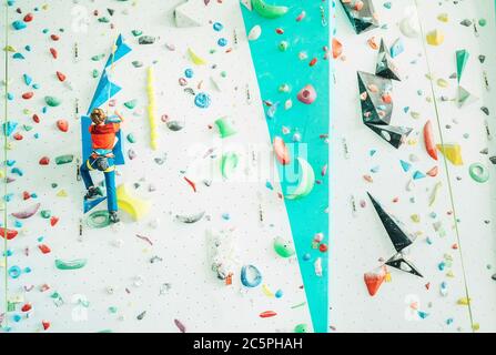 Teenager boy at indoor climbing wall hall. Boy is climbing using an auto belay system and climbing harness. Active teenager time spending concept imag Stock Photo