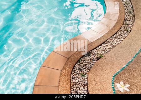 Curved swimming pool paved edge with pebbles. Clean transparent pool water waves background. Stock Photo