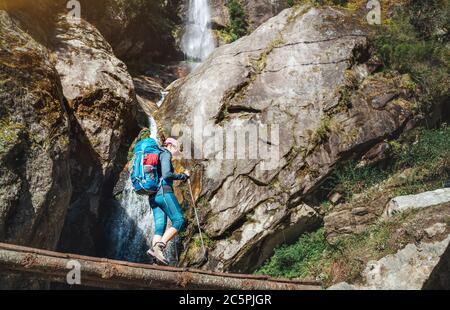 Young hiker backpacker woman using trekking poles hiking under the little waterfall on Everest Base Camp trekking route during high altitude Acclimati Stock Photo