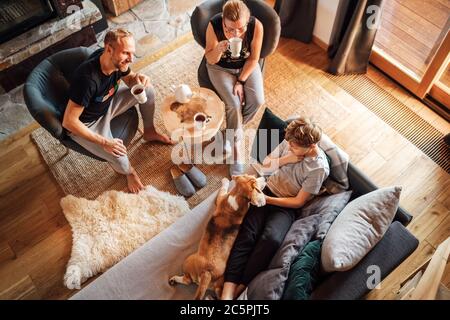 Cozy family tea time. Father, mother and son  at the home living room. Boy lying in comfortable sofa and  stroking their beagle dog and smiling. Peace Stock Photo