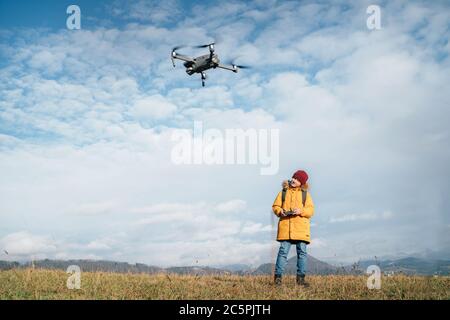 Teenager boy dressed yellow jacket piloting a modern digital drone using remote controller Stock Photo