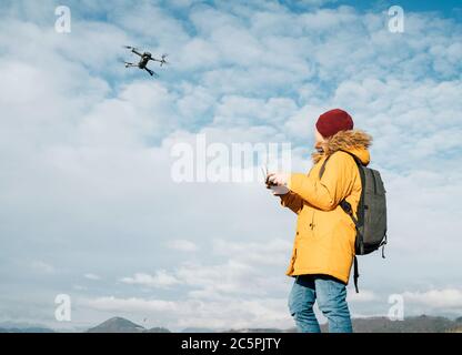 Teenager boy dressed yellow jacket piloting a modern digital drone using remote controller Stock Photo