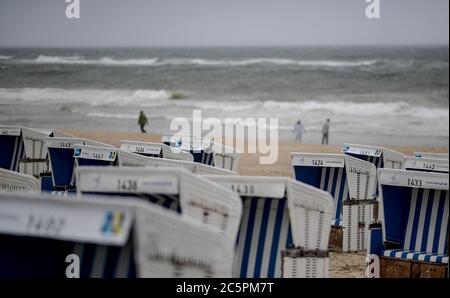 04 July 2020, Schleswig-Holstein, Westerland/Sylt: Walkers walk along the water and the beach chairs on Westerland beach. Photo: Axel Heimken/dpa Stock Photo