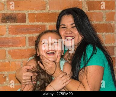 An Asian woman, in her 50th, and her daughter have a nice time together. Laughing and smiling. Red brick wall in the background Stock Photo