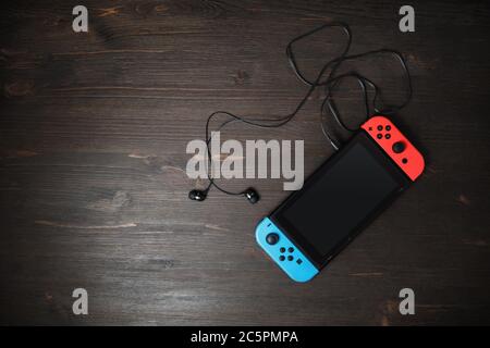 Minsk, Belarus - May 07, 2020: Nintendo Switch game console with blank black screen and headphones on wooden background. Copy space for text. Flat lay Stock Photo