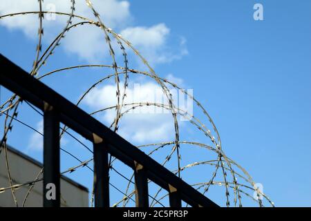 barbed wire fence of security or forbidden guarded area zone on blue sky with cluods with space for your text Stock Photo