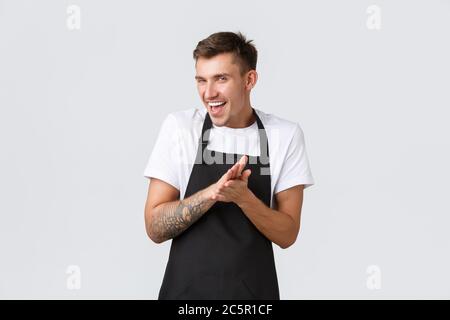 Small business owners, coffee shop and staff concept. Devious and smart funny barista in black apron, cafe worker rubbing hands as feeling relish or Stock Photo