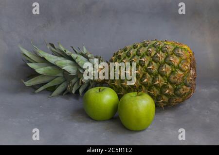 One whole pineapple with two green apples on gray background Stock Photo