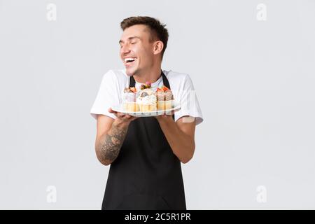 Small retail business, coffee shops and bakery concept. Handsome smiling barista, worker in store or waiter showing delicious desserts, selling tasty Stock Photo