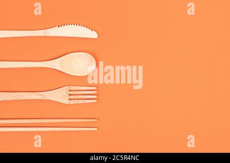 Reusable wooden cutlery. Eco friendly fork, knife, spoon on an orange background. Zero waste concept. Copyspace. Stock Photo