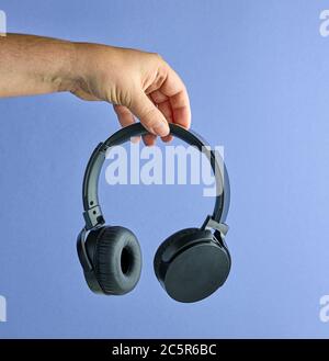 Black wireless headphones in human hand on blue background Stock Photo