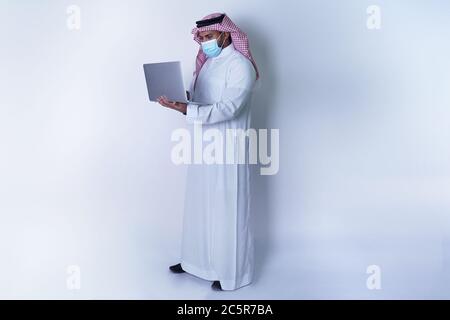 Saudi Arab Man standing and using laptop while wearing face mask Stock Photo