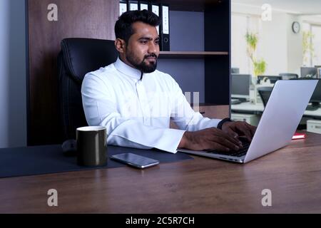 Saudi Arab Man sitting in cabin in office using laptop Stock Photo