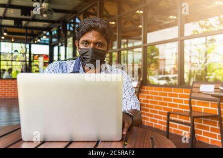 Happy Asian hand black man person sitting working with laptop computer, device technology and connecting networking online at the coffee cafe shop Stock Photo