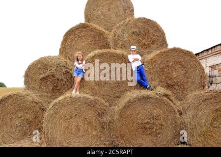 Two children are high under the sky on a haystack in the hay season. Stock Photo
