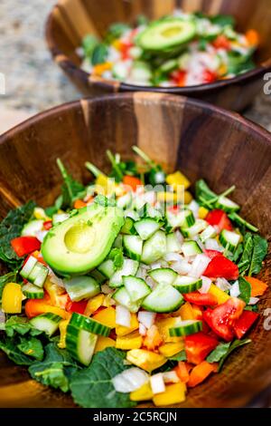 Chopped sliced vegetables in wooden bowls closeup with fresh vegan salad with baby kale, tomatoes, bell peppers and avocado half Stock Photo
