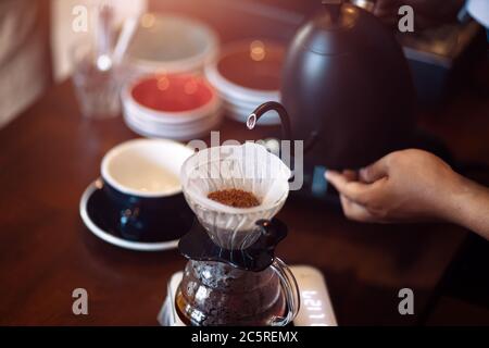 barista pouring boiling water from kettle to drip coffee maker. Stock Photo