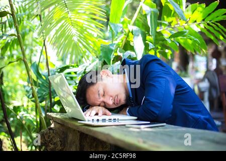 Tired businessman sleeping over a laptop in a desk at coffee shop. Stock Photo
