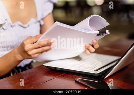 woman opening and reading a paper sheet near laptop on wooden table. Stock Photo