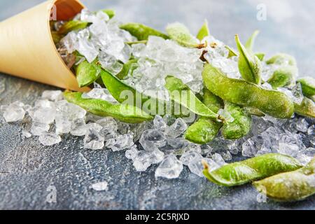 Frozen Edamame or soybeans in the mix with crushed ice on a blue background. Stock Photo