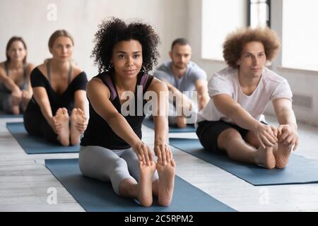 Sporty multiracial young people enjoying group yoga class in studio. Stock Photo