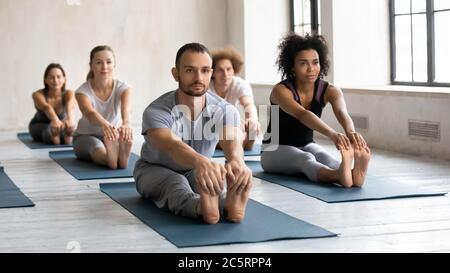 Multiracial people stretching muscles in seated forward bend pose. Stock Photo