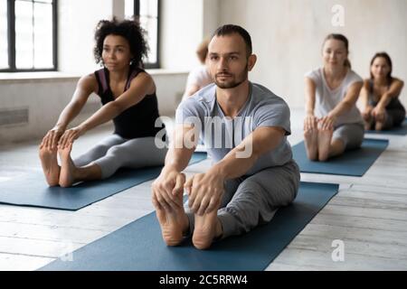 Focused professional male instructor leading yoga class in modern studio. Stock Photo